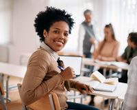 Happy black woman attends class at lecture hall and looks at camera.